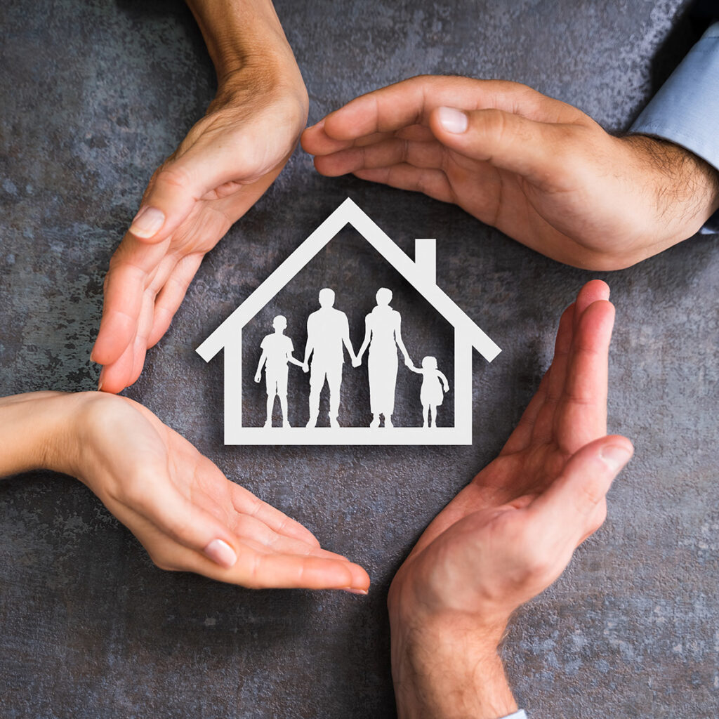 four hands encircling a paper cutout of a house with a family inside of it